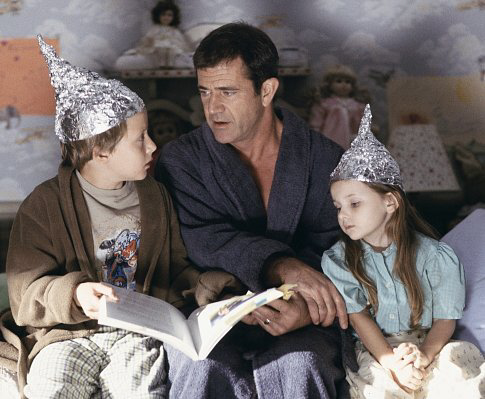 Graham (Mel Gibson, center) tries to calm his children, Morgan (Rory Culkin, left) and Bo (Abigail Breslin, right), who think that tin foil hats can stop aliens from reading their minds.